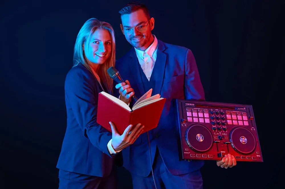 Traurednerin Julia Koch und Trauredner Robin Rehmann mit Traurede-Buch, Mikrofon und DJ-Controller